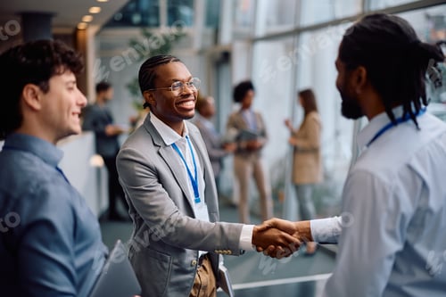 Preview: Happy black businessman shaking hands with his colleague while attending at convention center.