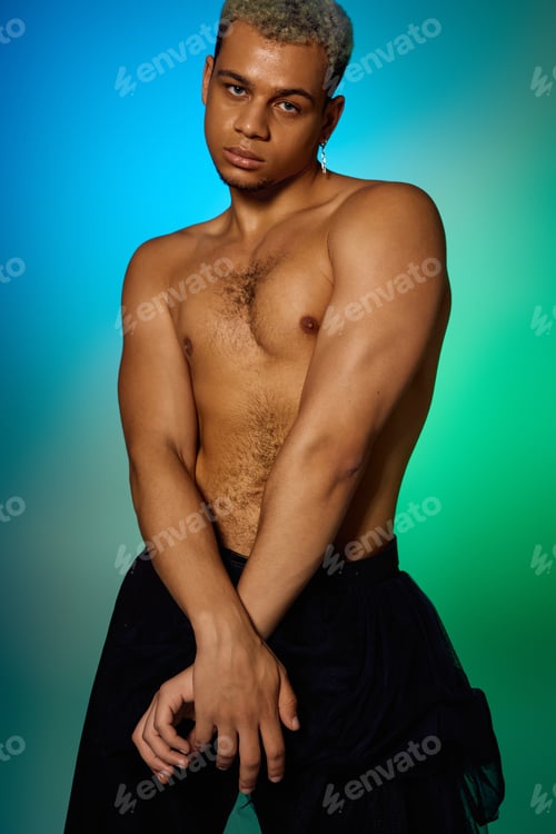 Preview: Stylish young man with dyed hair poses confidently in vibrant studio lighting