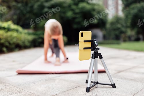 Preview: Cute Caucasian Kid seven-eight years old exercising online on fitness mat outdoor at summer day