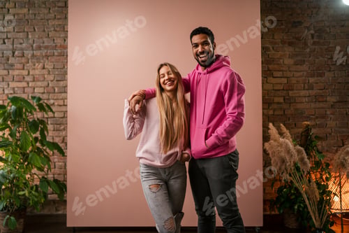 Preview: Fashion studio portrait of a happy young couple in hoodie posing over pink background.