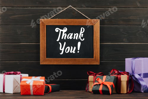Preview: thank you lettering on chalkboard in frame with gift boxes hanging on wooden wall