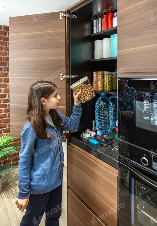 Preview: Young female organizing emergency food pantry in kitchen. 72 hours survival kit concept.