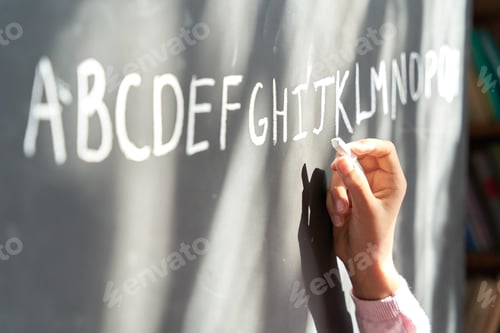 Preview: Hand of school girl pupil holding chalk writing english letters on blackboard.