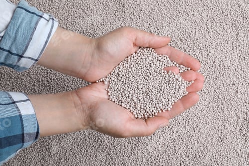 Preview: Woman holding chemical fertilizer over pellets, closeup. Gardening season