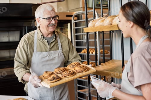 Preview: Senior man with buns and his daughter with tablet working in bakery