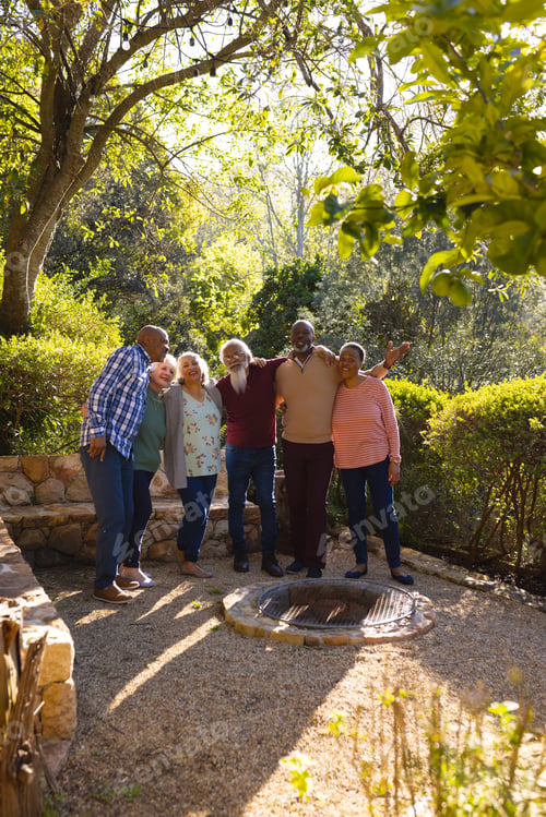 Preview: Happy diverse group of senior friends embracing and smiling in sunny garden