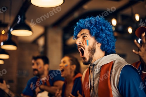 Preview: Excited sports fan screaming while watching a match with friends in bar.