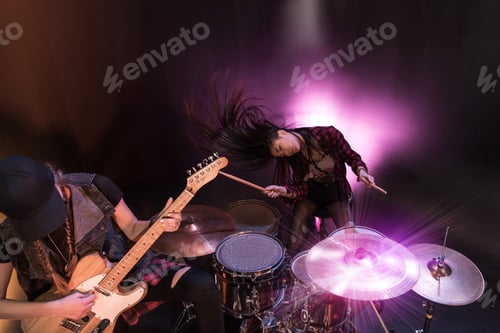Preview: Excited young women with drums set and electric guitar performing rock concert on stage