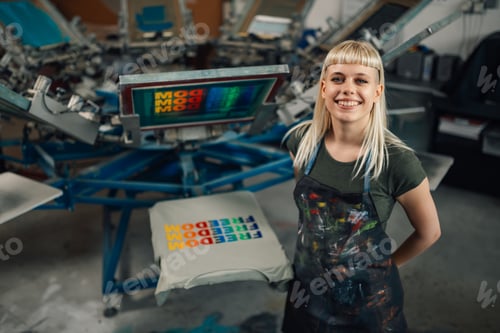 Preview: Happy print shop worker standing near screen printing press and smiling