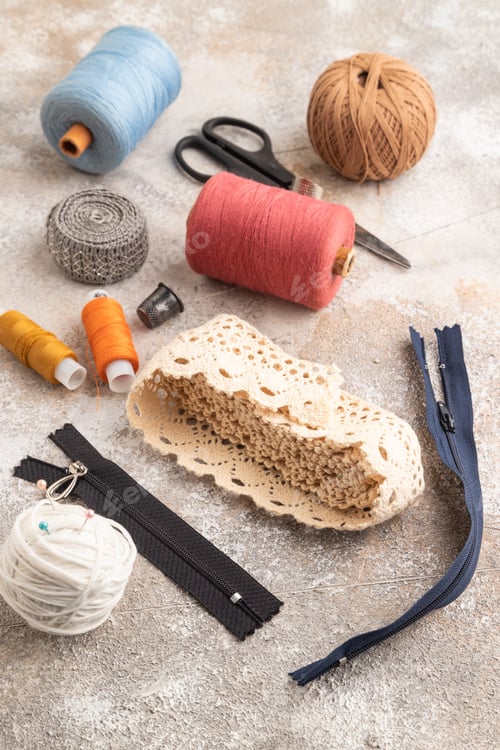 Preview: Sewing accessories: scissors, thread, thimbles, braid on brown concrete background. Side view