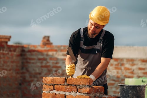 Preview: Placing the bricks, making a wall. A builder is working at the construction site at daytime