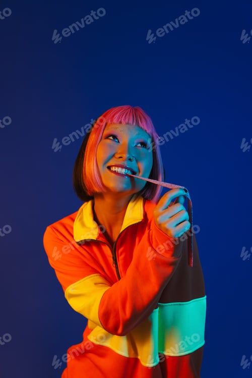 Preview: Asian girl with pink hair making fun while eating chewing marmalade