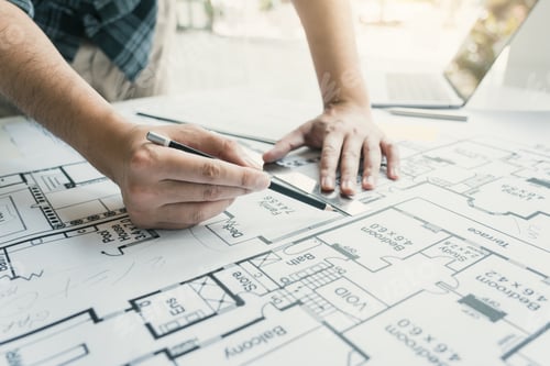 Preview: Interior designer or architect reviewing blueprints and holding pencil drawing on desk