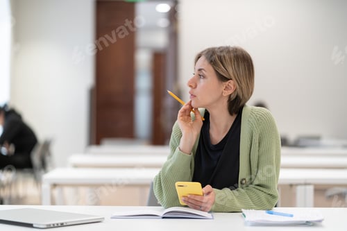 Preview: Mature female student taking second degree looking through window and dreaming, studying in library