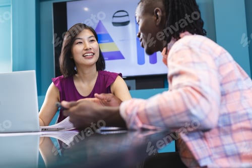 Preview: African American man and Asian woman are discussing over laptop in a modern business office