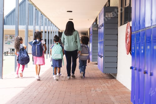 Preview: A biracial teacher walking with students in school hallway with blue lockers
