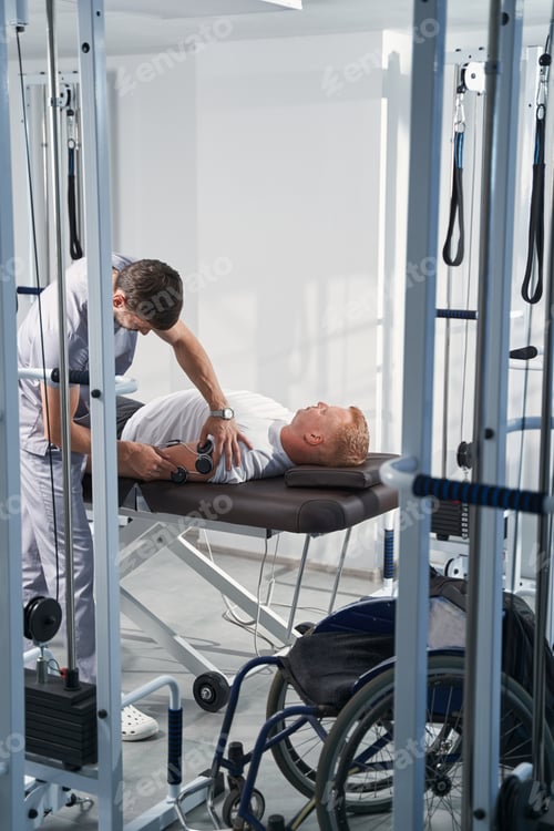 Preview: Therapist puts electrostimulator electrodes on man with disability arm