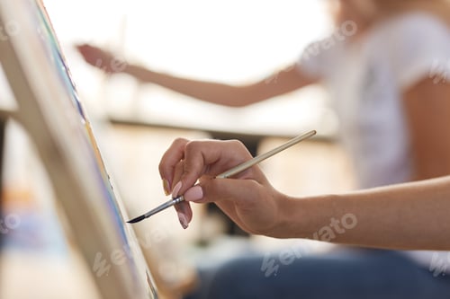 Preview: Girls hand holds a paint brush. Process of painting picture at the easels in the art studio