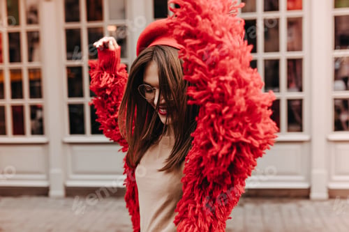 Preview: Active dark-haired girl in glasses is having fun on street. Woman in stylish beige top and red coat