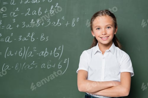 Preview: preteen schoolkid with crossed arms smiling at camera near equations on chalkboard