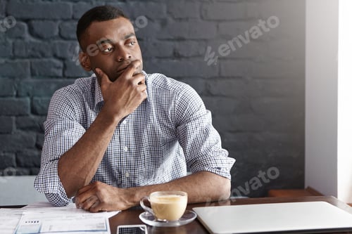 Preview: Thoughtful African businessman touching his chin, focused on finding new approaches and solutions in