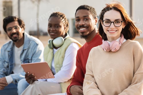 Preview: Cheerful millennial multiracial modern students use tablet for video lesson, have video call, study