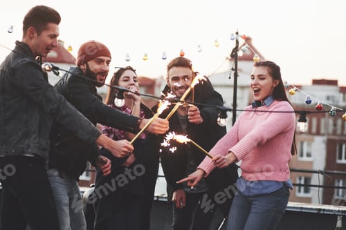 Preview: Feeling happy. Playing with sparklers on the rooftop. Group of young beautiful friends