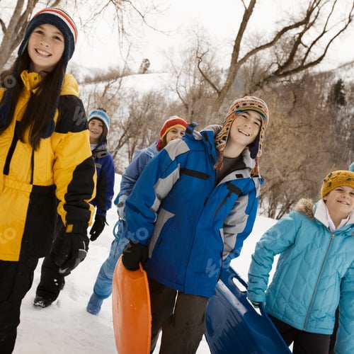 Preview: A group of children, boys and girls, carrying sledges across the snow.