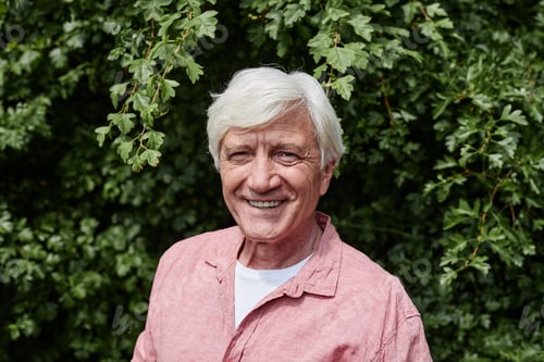 Preview: Smiling senior man looking at camera against greenery outdoors