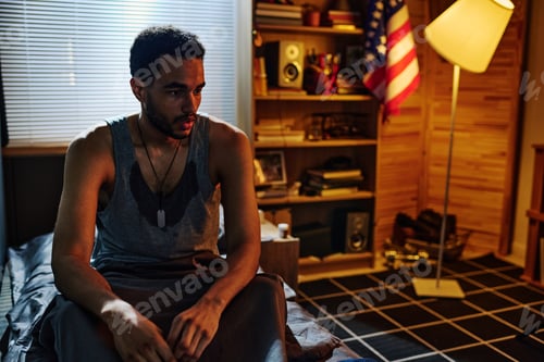 Preview: Young sweaty man in vest sitting on bed in the middle of the night