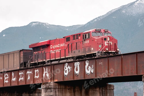 Preview: Train traveling across a picturesque bridge in front of a stunning mountainous landscape.