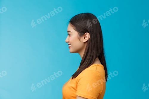 Preview: Profile shot asian cute woman perfect skin, turn left, smiling joyfully, pose near blue background