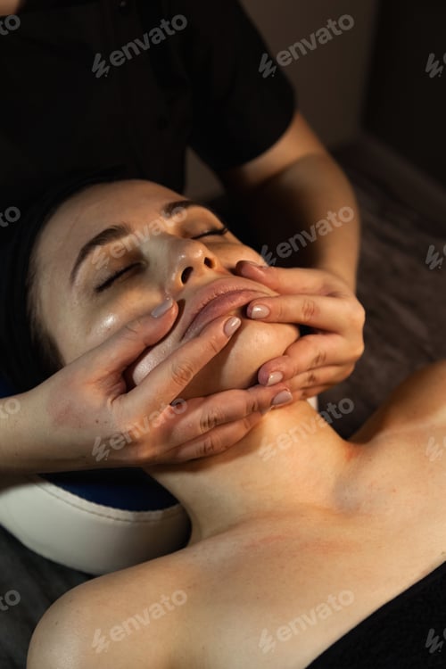 Preview: Close-up of woman masseur hands doing facial skin massage for beauty lady in medical spa salon