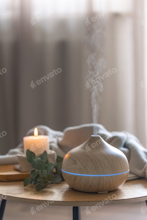 Preview: Wood aroma diffuser releasing mist in calm cozy interior with candle. Aromatherapy relaxation device