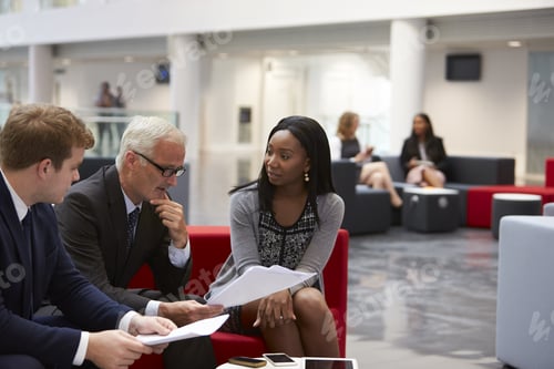 Preview: Businesspeople Discuss Document In Lobby Of Modern Office