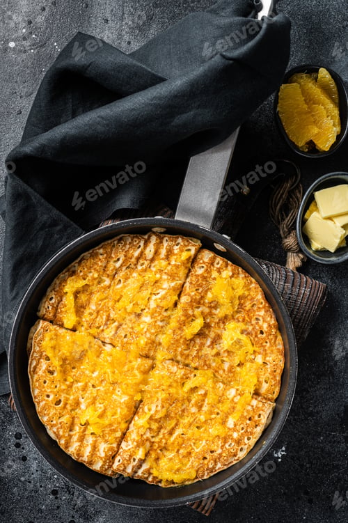 Preview: Cooking of French crepe Suzette with orange sauce in a skillet. Black background. Top view