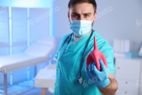 Preview: Doctor holding rubber enema in examination room, focus on hand. Space for text