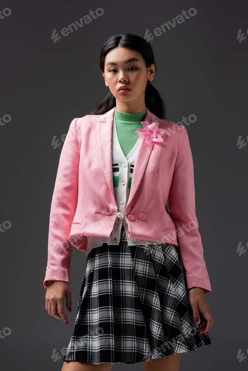Preview: Trendy asian woman in plaid skirt and pink jacket isolated on grey