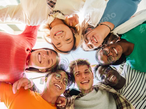 Preview: Low angle view of a group of multiracial friends standing on a circle, smiling and embracing