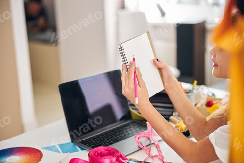 Preview: Joyful young stylist with a notepad sitting at the desk