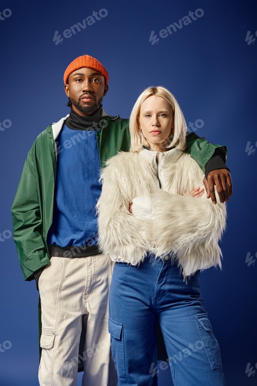 Preview: african american man hugging blonde woman in winter attire, diverse models standing on blue backdrop