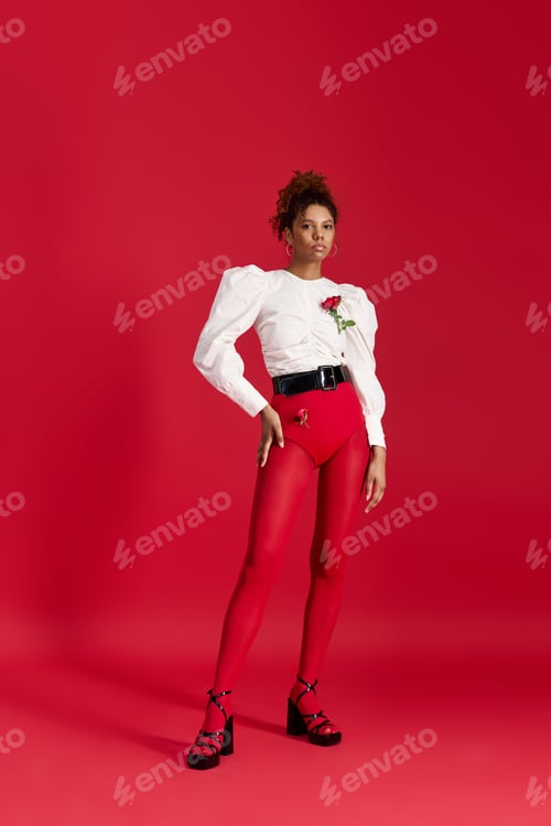 Preview: Striking young woman in fashionable red outfit poses confidently against vibrant backdrop