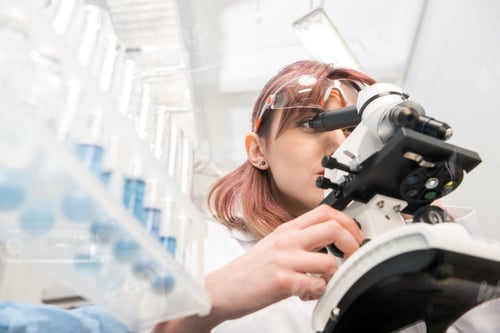 Preview: portrait of scientist in lab coat looking through microscope in laboratory