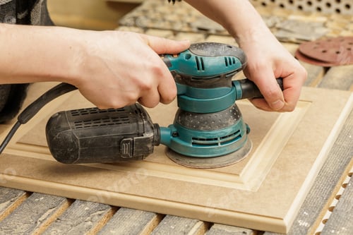 Preview: Hands using electric orbital sander to smooth wooden cabinet panel
