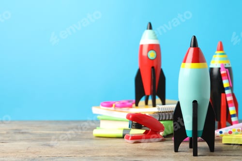 Preview: Bright toy rockets and school supplies on wooden table. Space for text