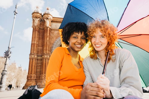 Preview: Two smiling women holding rainbow umbrella in barcelona, spain