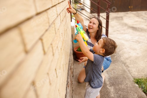 Preview: Mother and toddler son having fun playing in the backyard spraying with water guns