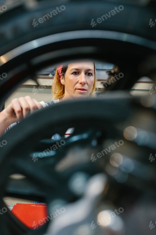Preview: Mechanic woman repairing motorcycle disk brake on factory