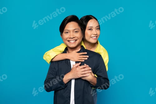 Preview: Cheerful young japanese woman hug man in casual look at free space
