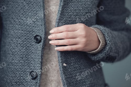 Preview: Close-up of a gray knitted jacket and a woman's hand. Winter, autumn warm woolen clothes.